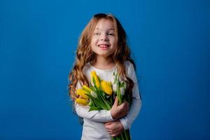 ritratto di un' affascinante sorridente poco ragazza con un' mazzo di tulipani nel sua mani. stile di vita. fresco fiori. internazionale Da donna giorno. spazio per testo. alto qualità foto