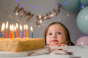 carino poco ragazza colpi su candele su un' compleanno torta a casa contro un' fondale di palloncini. del bambino compleanno foto