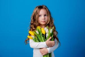 ritratto di un' affascinante sorridente poco ragazza con un' mazzo di tulipani nel sua mani. stile di vita. fresco fiori. internazionale Da donna giorno. spazio per testo. alto qualità foto