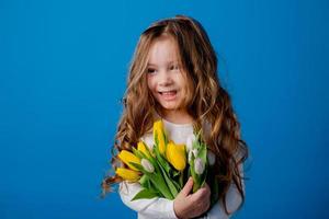 ritratto di un' affascinante sorridente poco ragazza con un' mazzo di tulipani nel sua mani. stile di vita. fresco fiori. internazionale Da donna giorno. spazio per testo. alto qualità foto