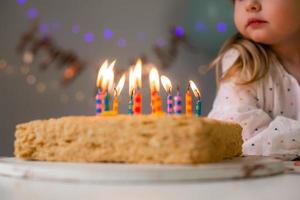 carino poco ragazza colpi su candele su un' compleanno torta a casa contro un' fondale di palloncini. del bambino compleanno foto