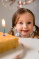 carino poco ragazza colpi su candele su un' compleanno torta a casa contro un' fondale di palloncini. del bambino compleanno foto