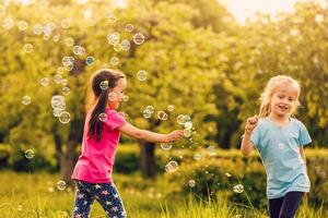 Due ragazze siamo contento di il galleggiante sapone bolle nel natura foto