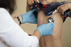 il medico usi un' stetoscopio su il ragazzi stomaco per dai un'occhiata il suo Salute. foto