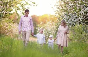 contento genitori mamma e papà, figlia e figlio, giovane famiglia all'aperto nel primavera contro il fondale di fioritura Mela e ciliegia alberi foto