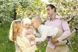 contento genitori mamma e papà, figlia e figlio, giovane famiglia all'aperto nel primavera contro il fondale di fioritura Mela e ciliegia alberi foto