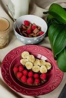 colazione, cereale con latte, caffè con latte nel un' sfaccettato bicchiere, beterbrots con cioccolato Burro, frutti di bosco e banane foto