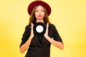 ragazza nel un' nero completo da uomo su un' giallo sfondo con un' disco nel sua mani, musica, il ragazza Spettacoli emozioni foto