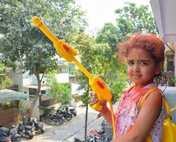 dolce poco indiano ragazza giocando colori su holi Festival, Tenere pichakaree pieno di colori, holi Festival celebrazioni nel delhi, India foto