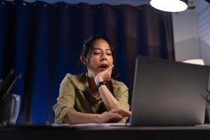 asiatico donna sentire assonnato e opera con il computer portatile computer a notte, Lavorando sovraccarico. foto