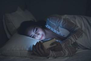 asiatico donna giocando gioco su smartphone nel il letto a notte, Tailandia persone, tossicodipendenti sociale media foto