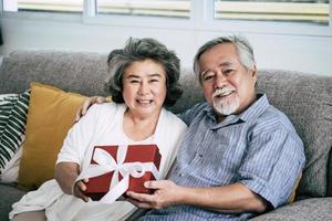 sorprese coppia di anziani con confezione regalo in soggiorno