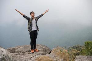 escursionista con zaino in piedi sulla cima di una montagna con le mani alzate foto
