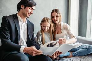 contento poco ragazza legge un' libro con sua genitori foto