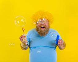 stupito uomo con giallo parrucca nel testa giocare con bolle sapone foto