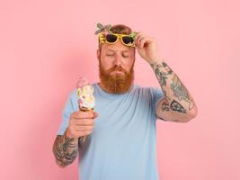 riflessivo uomo con barba e tatuaggi mangia un' grande gelato foto