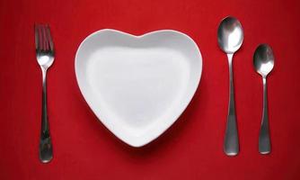 cuore forma piatto cucchiaio e forchetta su rosso sfondo foto