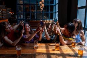 gruppo di sorridente femmina amici prendere un' autoscatto con un' smartphone mentre potabile birra nel un' pub foto