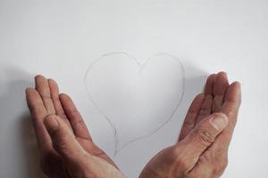 la mano di un giovane che si prende cura di una forma di cuore scritta a mano da una matita foto