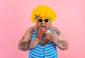 Grasso uomo con barba e parrucca mangia un' ghiacciolo e un gelato foto