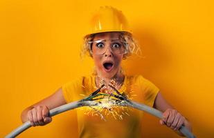 lavoratore ragazza con cappello pause un elettrico cavo. giallo sfondo foto