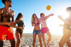 gruppo di amici giocando a spiaggia volley a il spiaggia foto