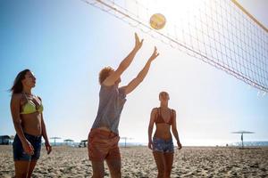 gruppo di amici giocando a spiaggia volley a il spiaggia foto