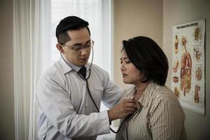 medico nel bianca uniforme toga ascolta polmone e cuore paziente con stetoscopio foto