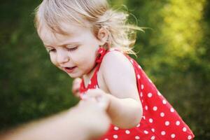 ritratto di un' poco contento ragazza. il bambino detiene il mano di il genitore e giochi foto