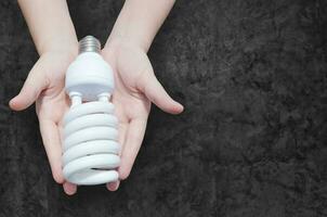 energia Salvataggio concetto, donna mano Tenere leggero lampadina su buio sfondo, idee leggero lampadina nel il mano foto