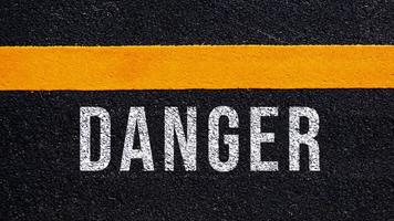 Pericolo scritto e giallo linea su il strada nel mezzo di il asfalto strada, Pericolo parola su strada. foto