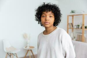 bellissimo africano americano ragazza con afro acconciatura a casa interno. giovane africano donna con Riccio capelli nel vivente camera. bellezza etnico le persone, domestico vita concetto. foto