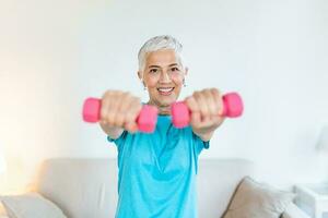 anziano donna esercizio con manubri a casa. sportivo bellissimo donna esercizio a casa per restare in forma. anziano donna esercizio a casa nel un' vivente camera. fitness, allenarsi foto