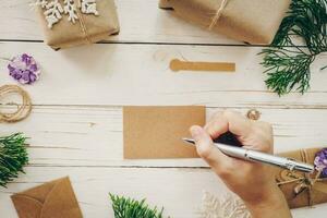 vicino su di mani donna scrittura vuoto Lista dei desideri e Natale carta su di legno tavolo con natale decorazione. foto