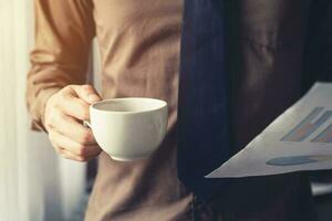 attività commerciale uomo mano Tenere caffè tazza e carta foglio a finestra nel ufficio. foto