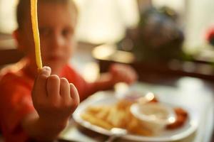 ragazzo mangiare veloce cibo nel un' bar. il bambino mangiare francese patatine fritte con pepite foto