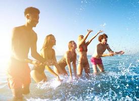 gruppo di amici avendo divertimento a il spiaggia con acqua mare foto