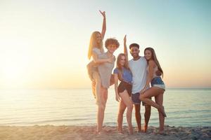 gruppo di contento amici avendo divertimento a oceano spiaggia a alba foto