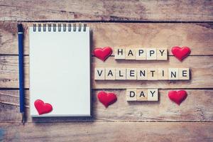 vuoto taccuino e legna testo per contento San Valentino giorno con rosso cuore su legna sfondo. foto