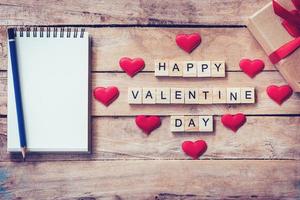 vuoto taccuino, regalo scatola e legna testo per contento San Valentino giorno con rosso cuore su legna sfondo. foto