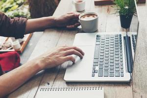 attività commerciale uomo digitando il computer portatile e Tenere caffè tazza su legna tavolo. foto