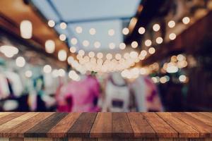 vuoto di legno tavolo e sfocato sfondo a notte mercato Festival persone a piedi su strada con copia spazio, Schermo montaggio per Prodotto. foto