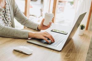 donna utilizzando il computer portatile e Tenere caffè Lavorando su di legno tavolo foto