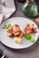 rotoli di fritte Bacon e schiacciato patate e basilico su un' piatto su il tavolo. verticale Visualizza foto