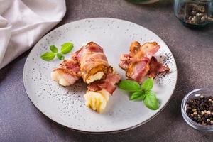 rotoli di fritte Bacon e schiacciato patate e basilico su un' piatto su il tavolo. foto