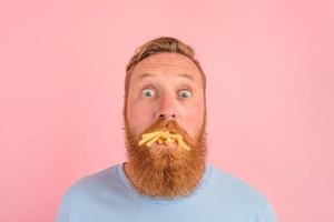 Affamato uomo con barba e tatuaggi mangia fritte patate foto