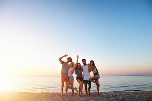 gruppo di contento amici avendo divertimento a oceano spiaggia a alba foto