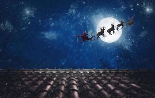 Santa Claus su il suo slitta, tirato di renna, volante a notte per consegnare i regali foto