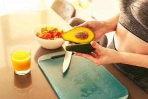 donna nel il casa cucina taglio un avocado per un' salutare mangiare foto