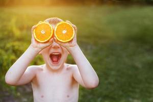 bambino con metà di arance su occhi. contento bambino avendo divertimento e mostrando lingua foto